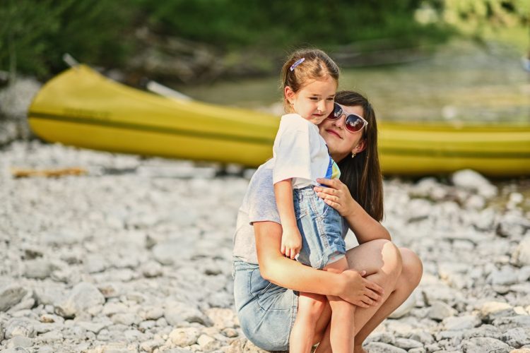 Mother with daughter against canoe in rocky shore of a calm river